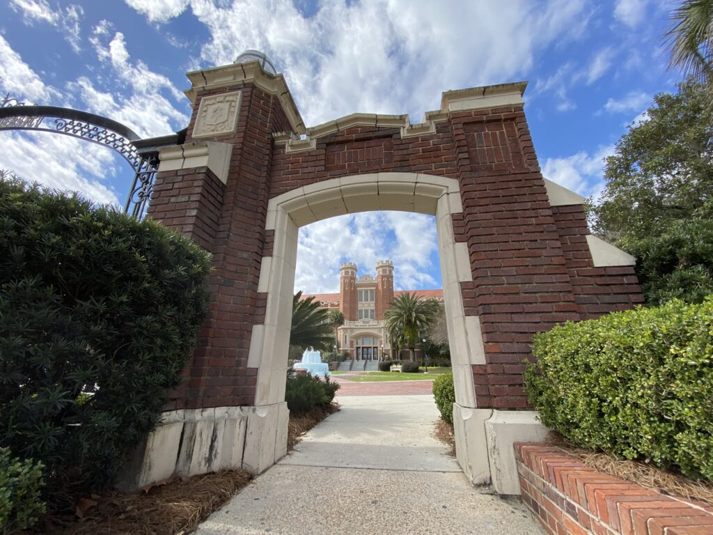 The entrance gate to the Westcott Building at FSU, with the building and fountain showing through the Entrance doorway on a sunny, blue sky day