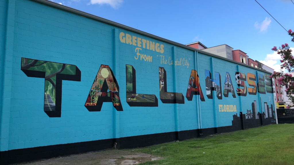 Blue mural featuring the letters of Tallahassee, with each letter representing a different piece of Tallahassee history, in railroad square 