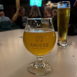 Amicus beer glass on a table at their taphouse, with another beer glass in the background