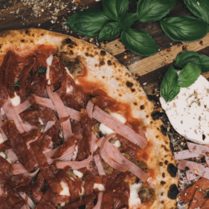 La carne pizza from Isabella's in Tallahassee, on a table with fresh basil and mozzarella next to it.  